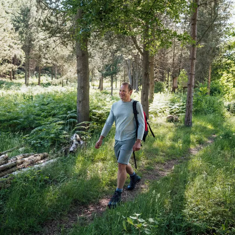 A wide-shot of a caucasian male in his 50's walking in the countryside and taking in his surroundings.
